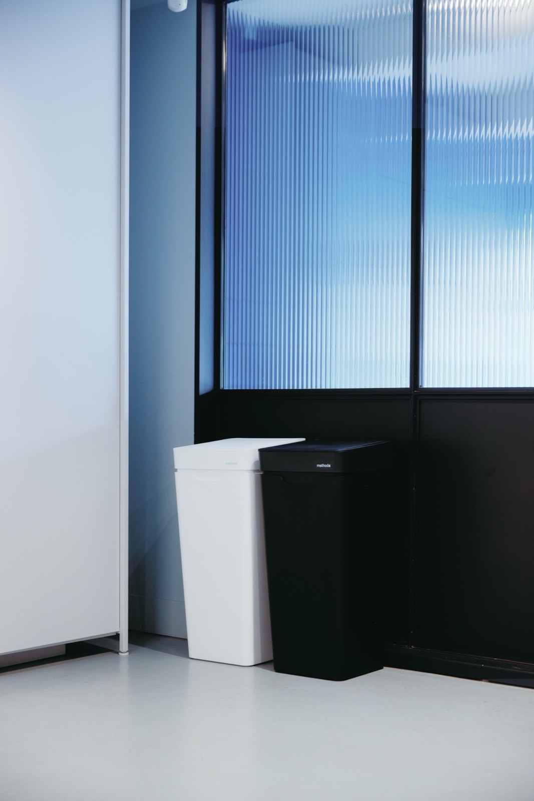 A white Mono and a black Mono side by side in front of fluted blue glass