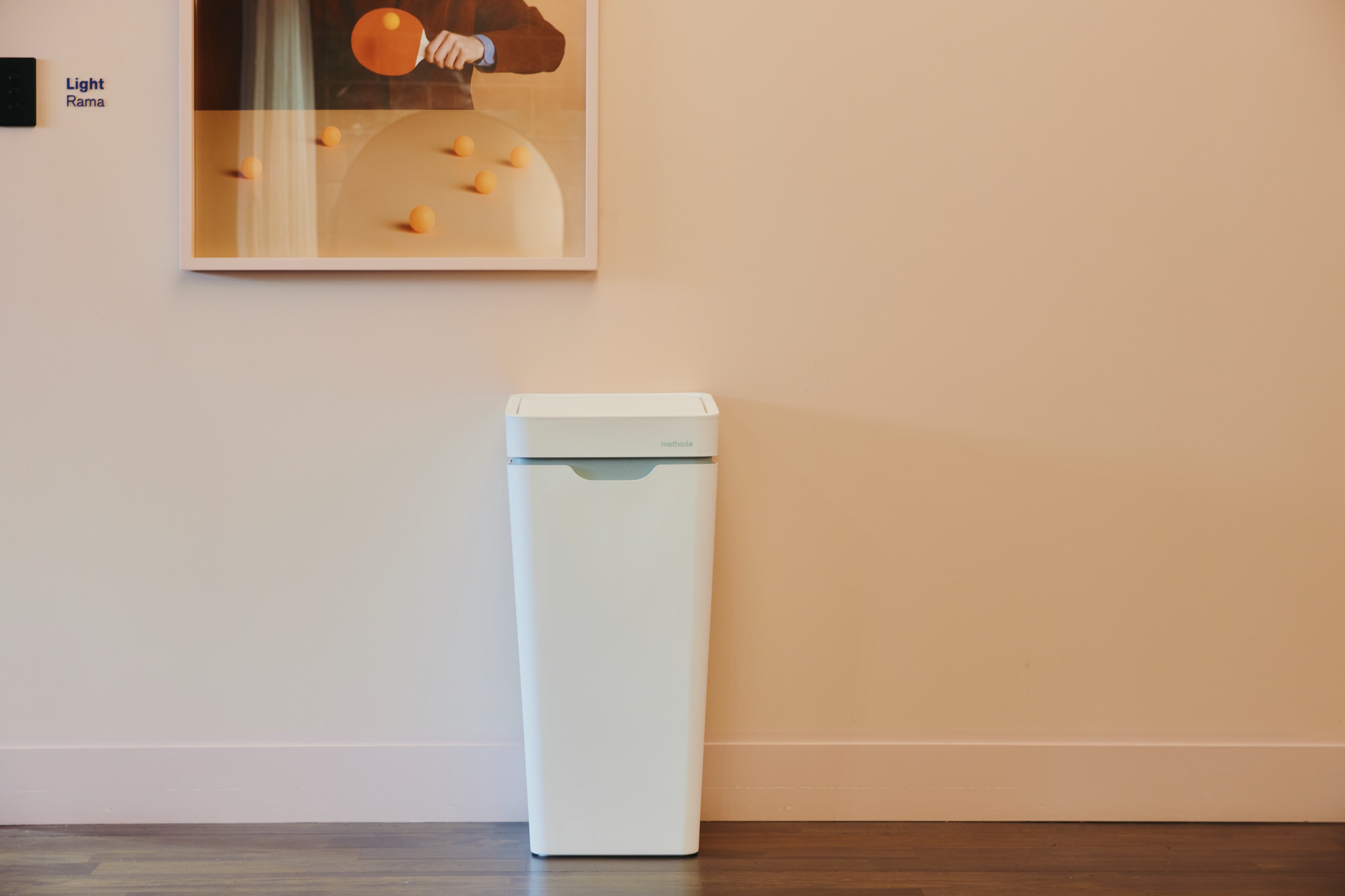 A white Mono against a pale pink wall below a framed print